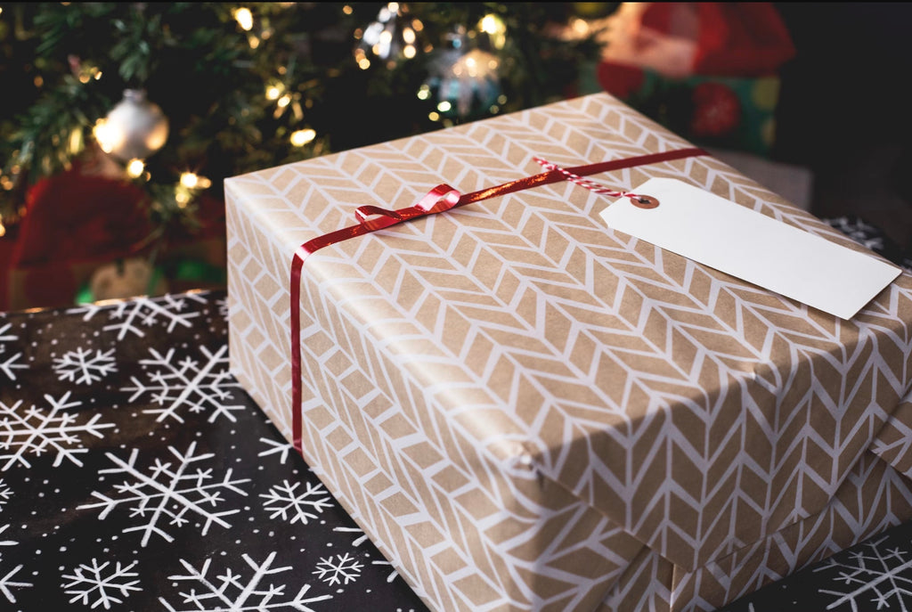 A present wrapped up with a bow in front of the Christmas tree