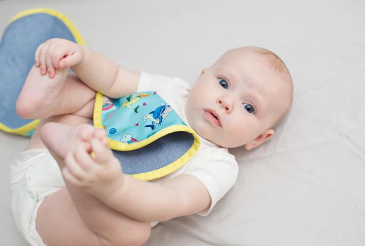 a baby grabbing his feet with a reusable cloth over him