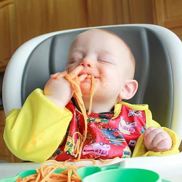 a baby with a bib eating spaghetti