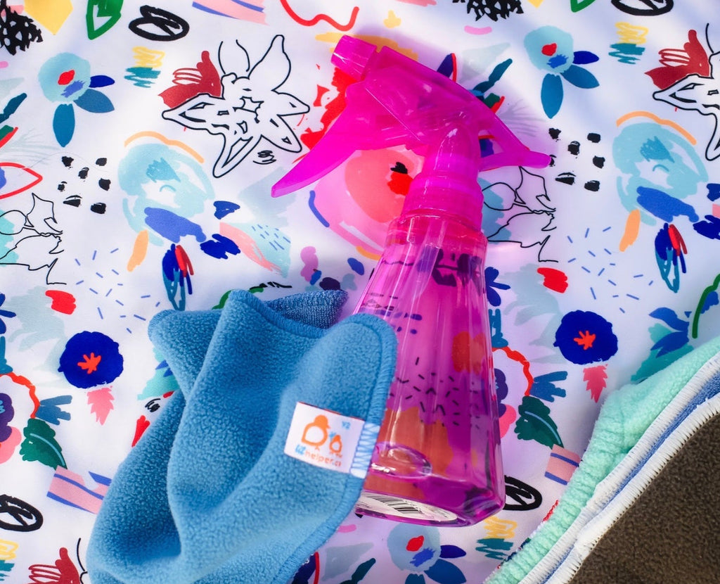Pink spray bottle and blue mitt on a colorful fabric background