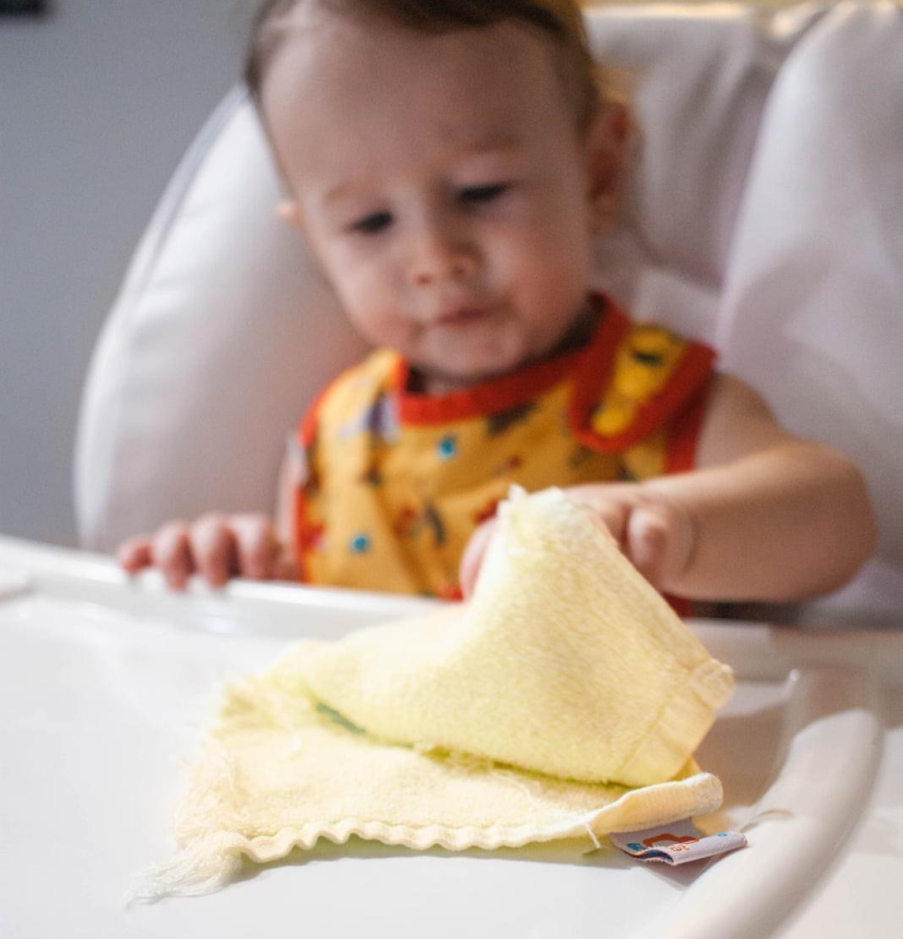 a baby in a high-chair grabbing a cloth wipe